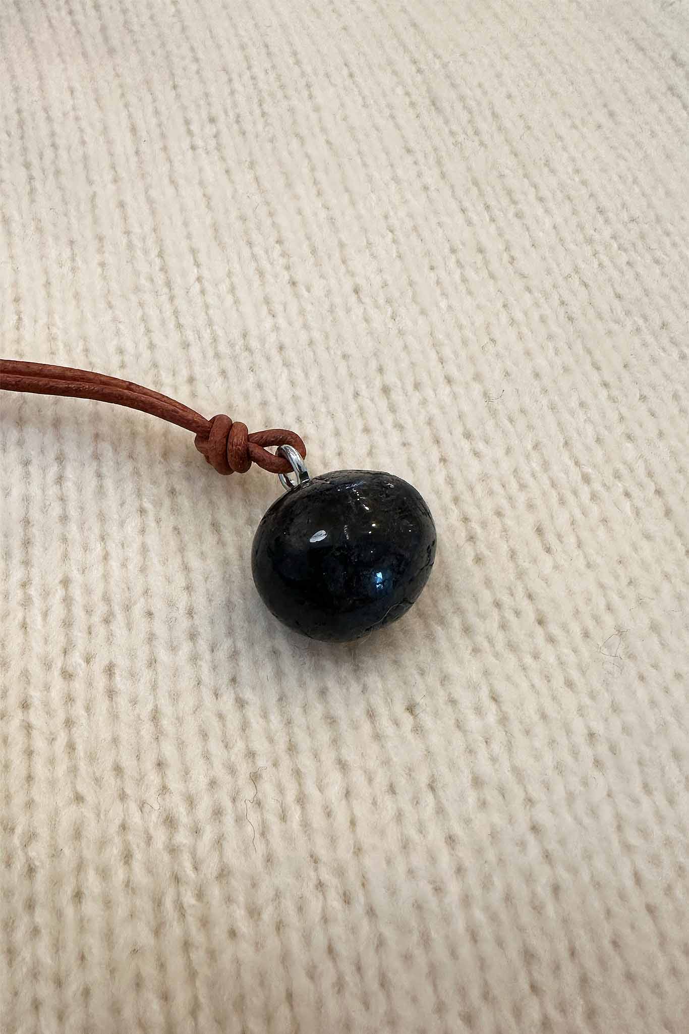 Round natural garnet pendant on a brown cord against a beige fabric background