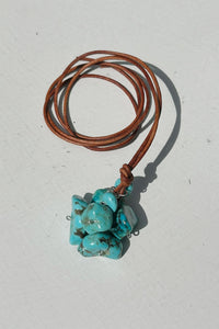 Turquoise stone pendant cluster on a brown leather cord against a white background