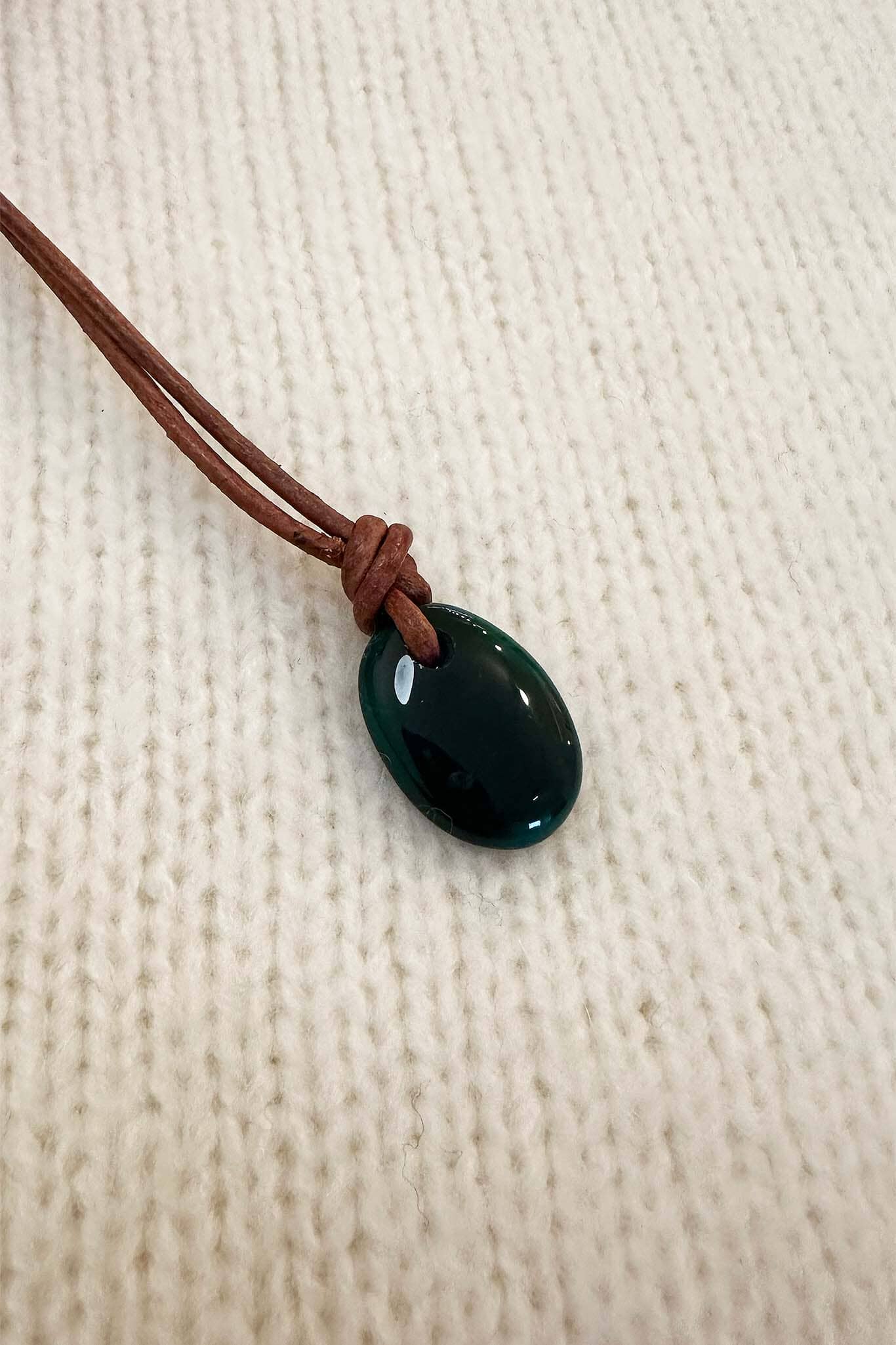 Green oval onyx pendant on a brown cord against a beige fabric background