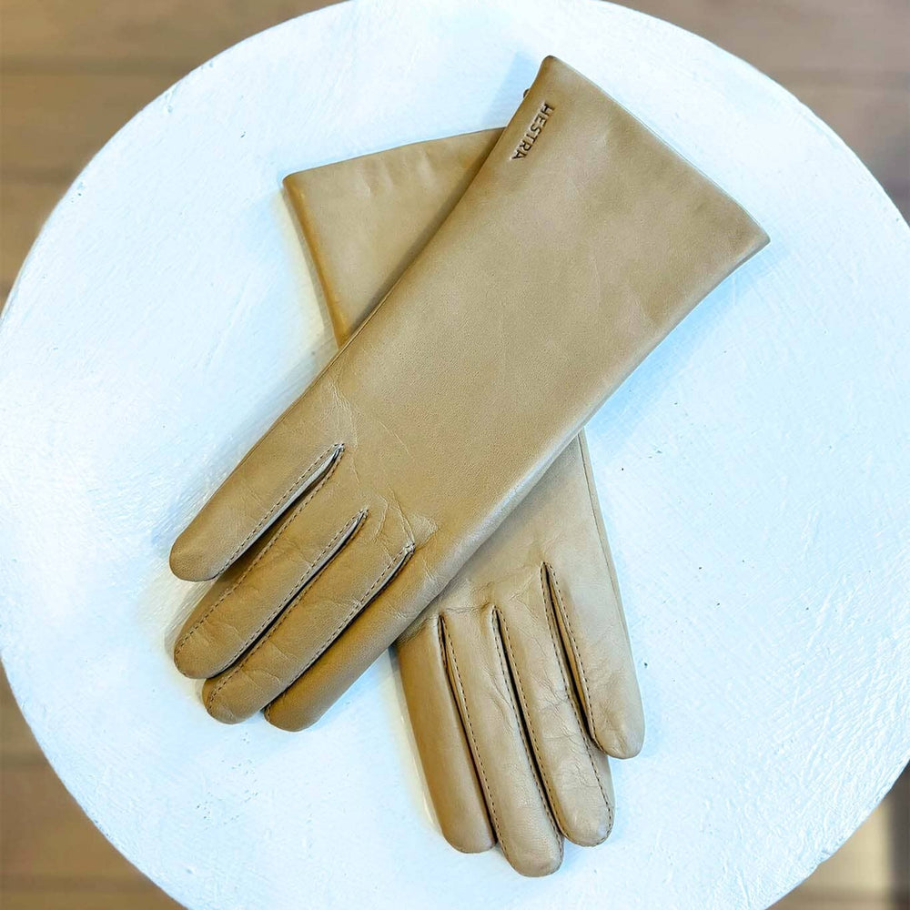 
                  
                    Pair of beige gloves on a white surface with a wooden background
                  
                