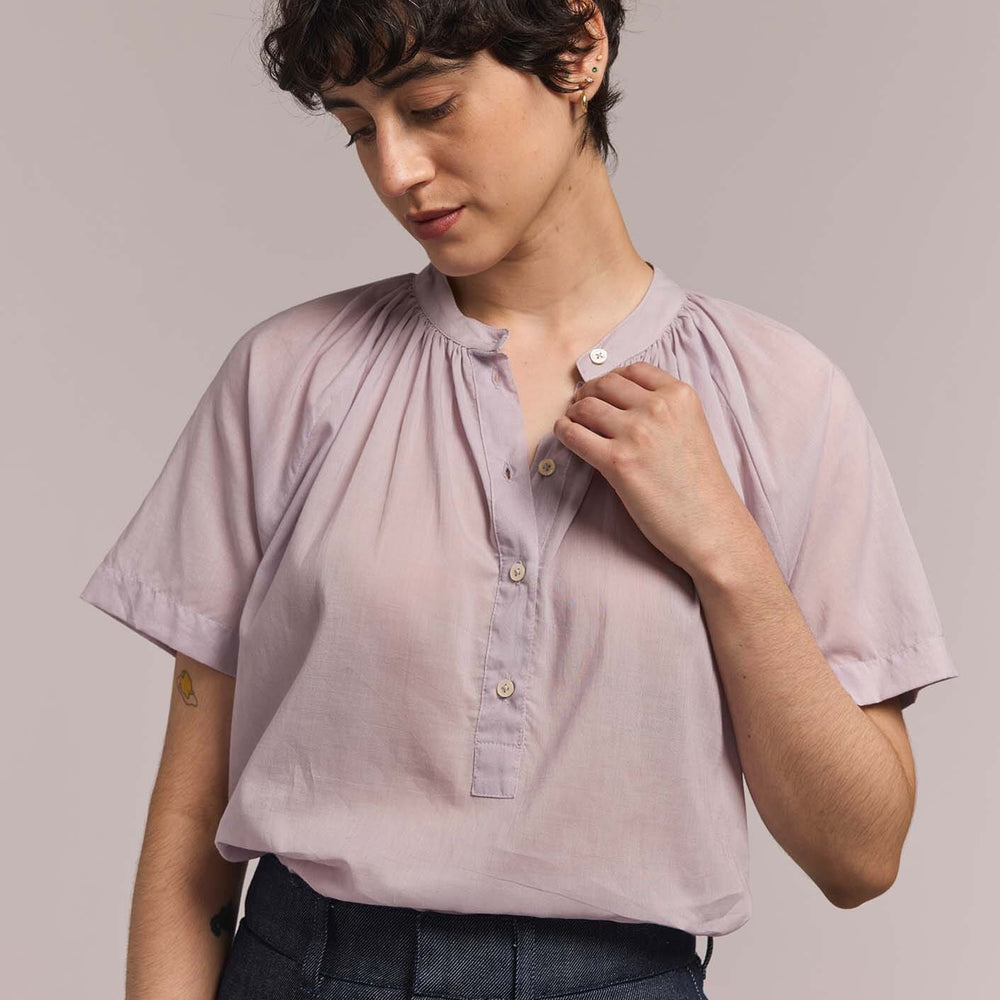 Woman wears a light purple blouse with a plain background