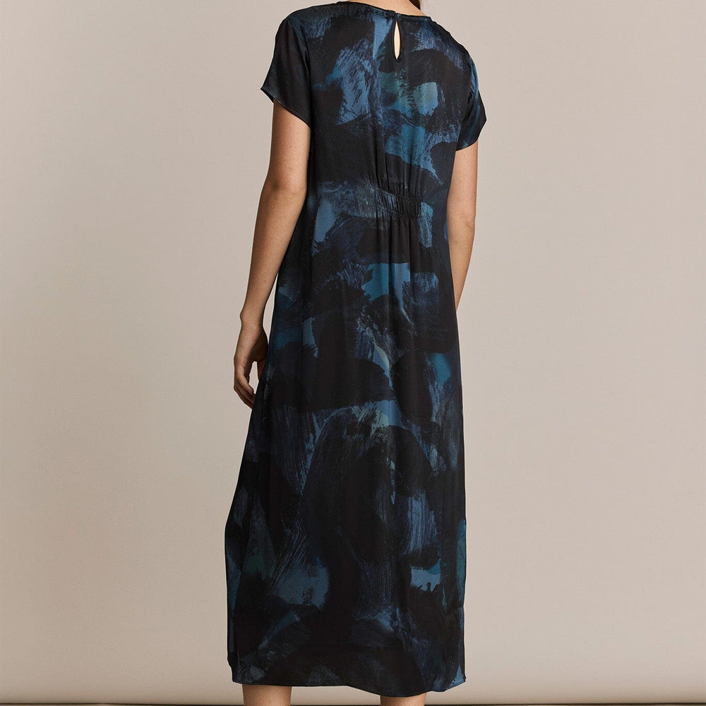 Woman wearing a blue patterned silk short sleeve dress against a beige background