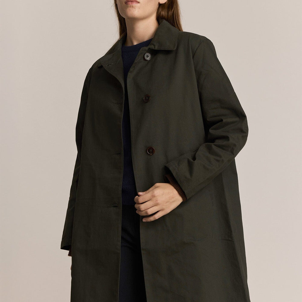
                  
                    Woman wearing a dark green trench coat and black pants against a plain background
                  
                