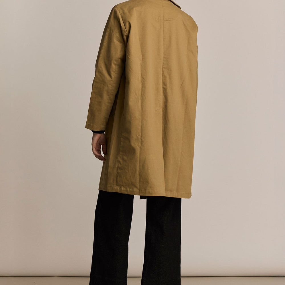 Person wearing a beige trench coat against a plain background