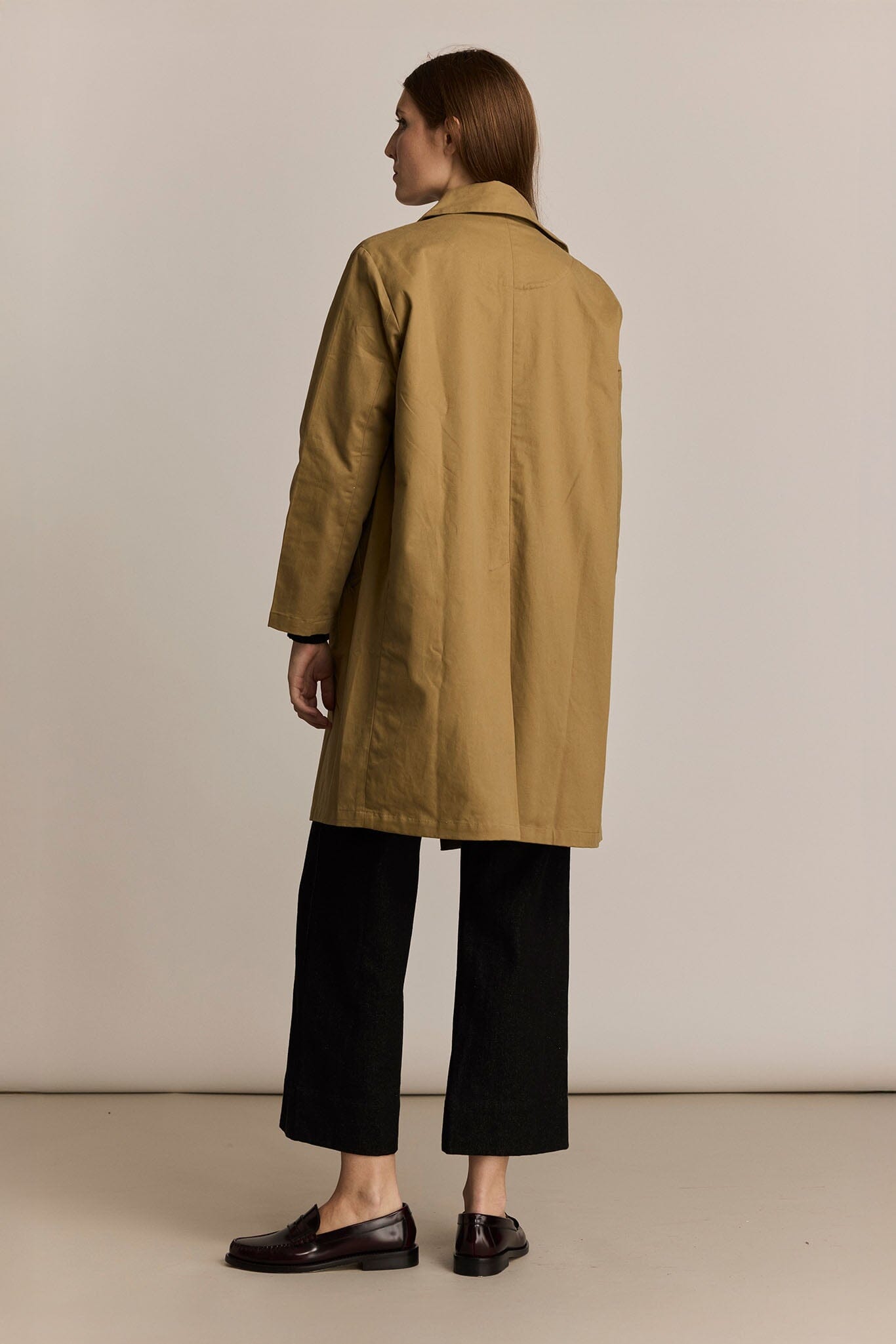 Person wearing a beige trench coat against a plain background