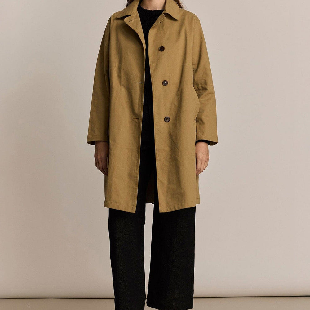 Woman wearing a beige trench coat against a plain background