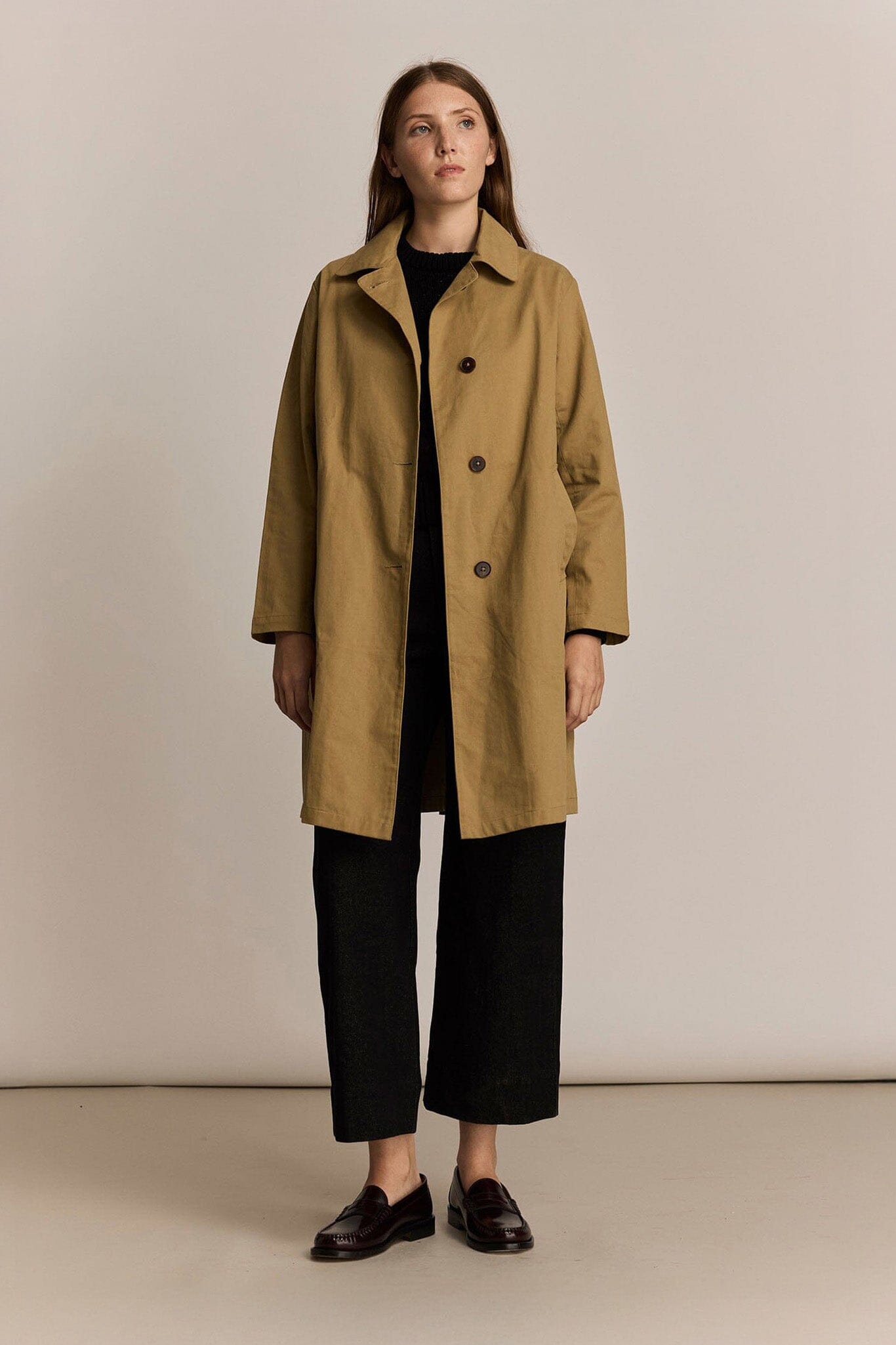Woman wearing a beige trench coat against a plain background