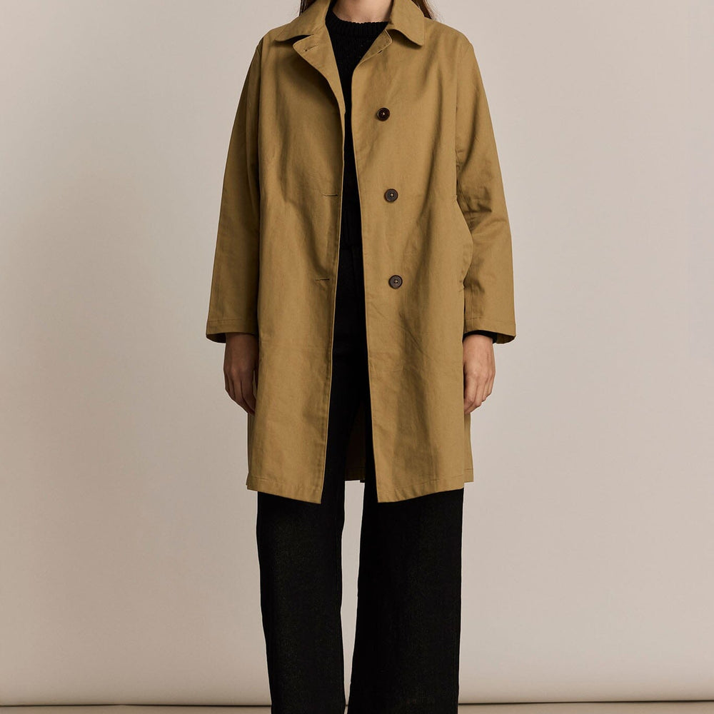 Woman wearing a beige trench coat against a plain background