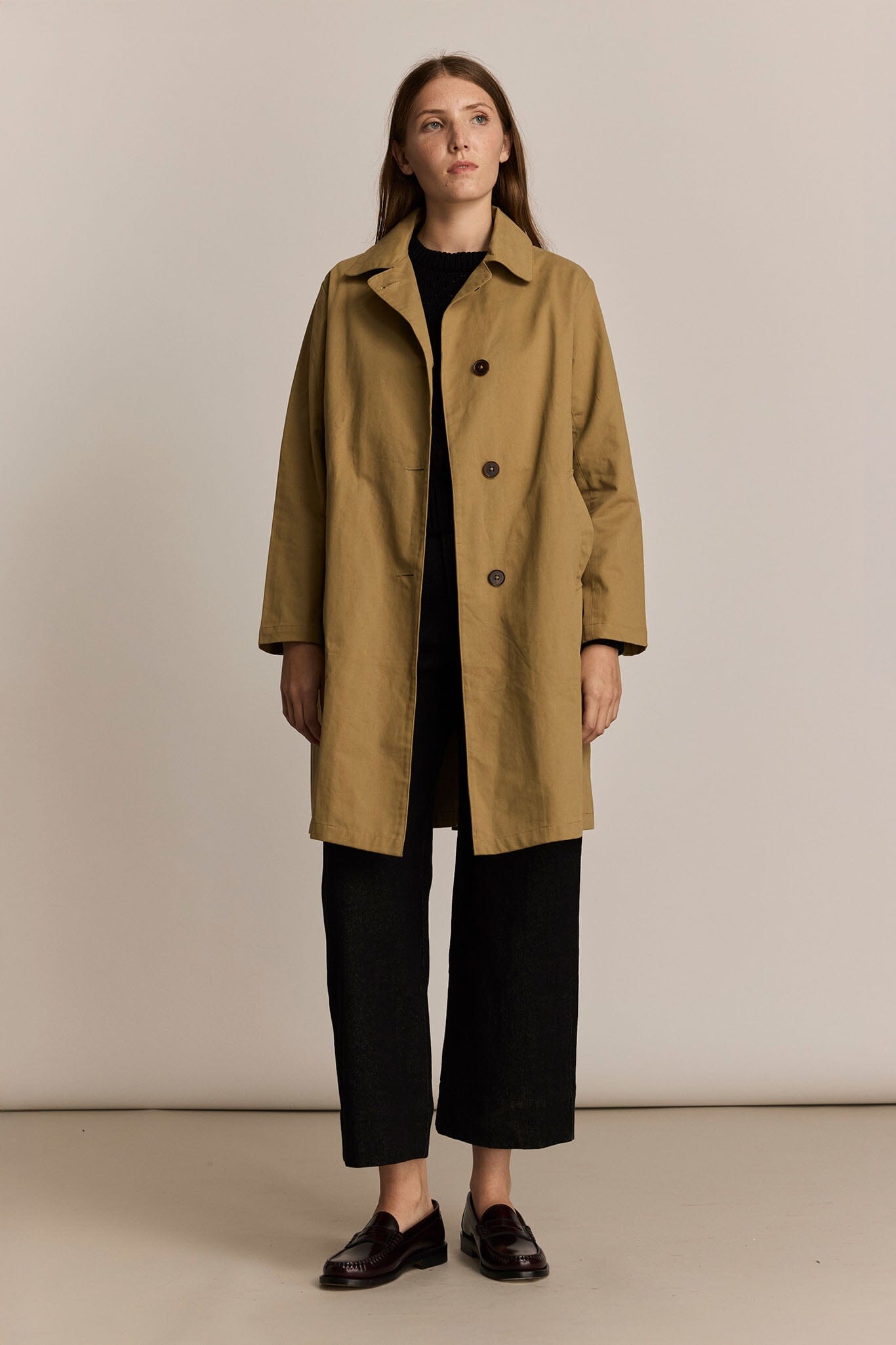 Woman wearing a beige trench coat against a plain background
