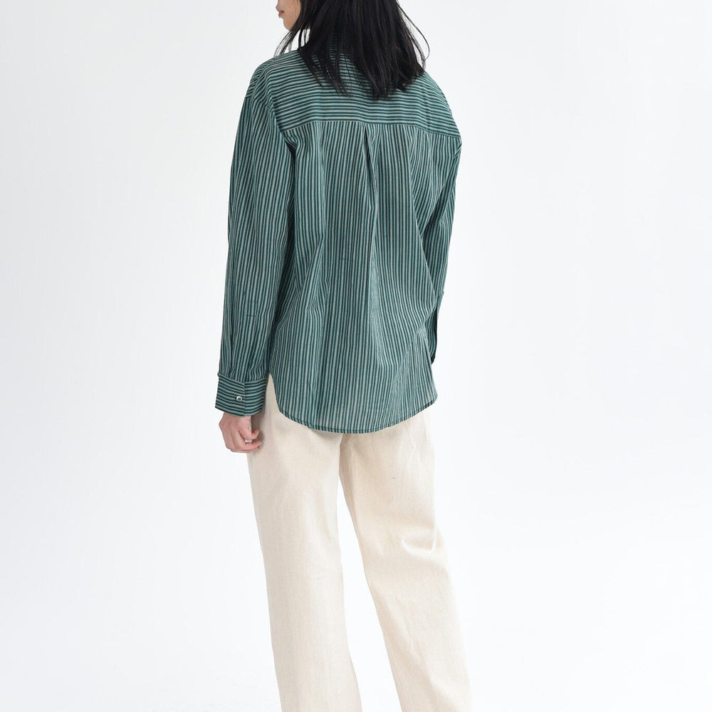 A woman wears a dark green, striped long sleeve button down blouse.