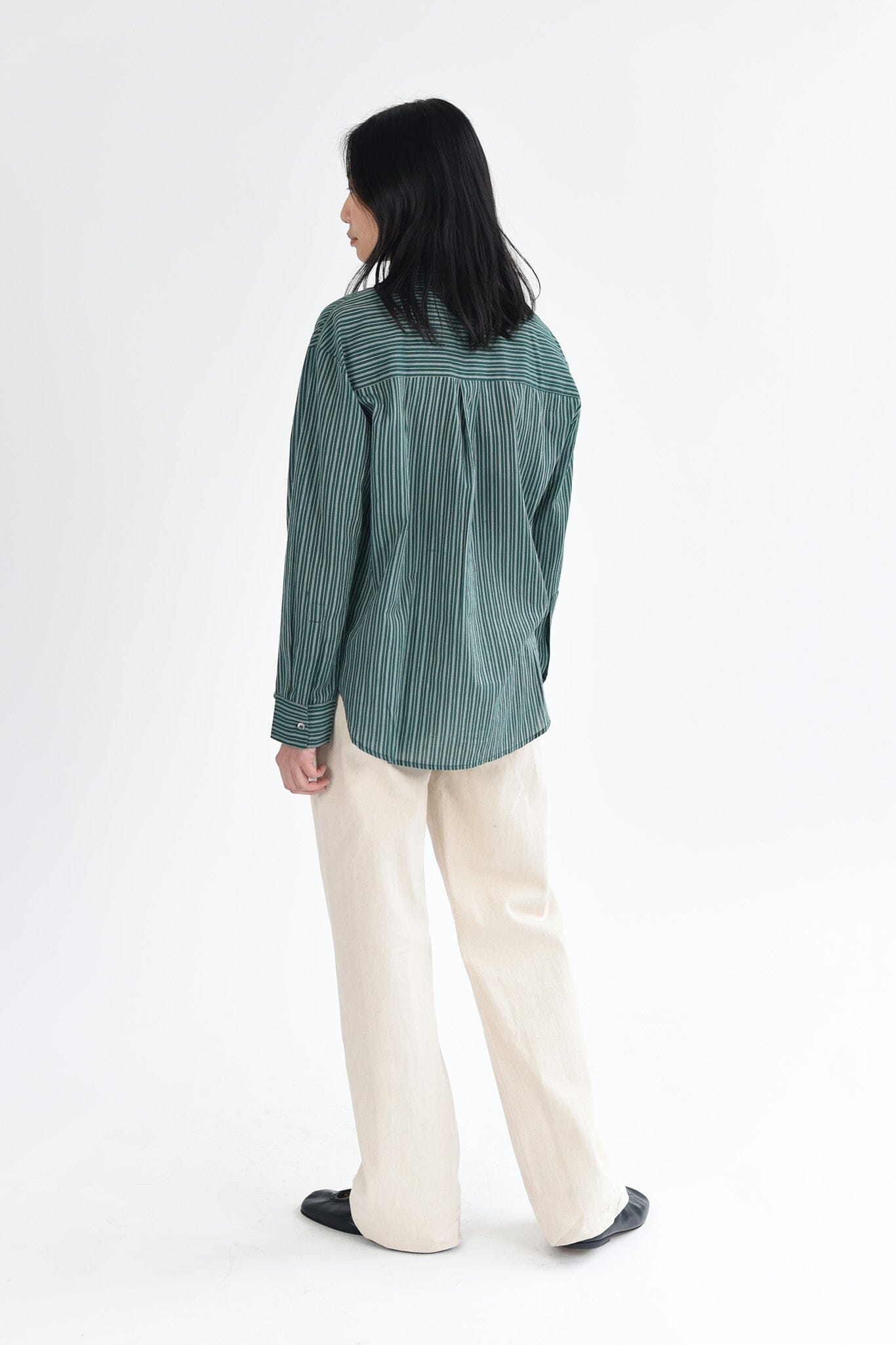 A woman wears a dark green, striped long sleeve button down blouse.