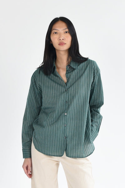 A woman wears a dark green, striped long sleeve button down blouse. The top is lightweight and made of cotton. Available to purchase at M.Patmos in Brooklyn, New York. 