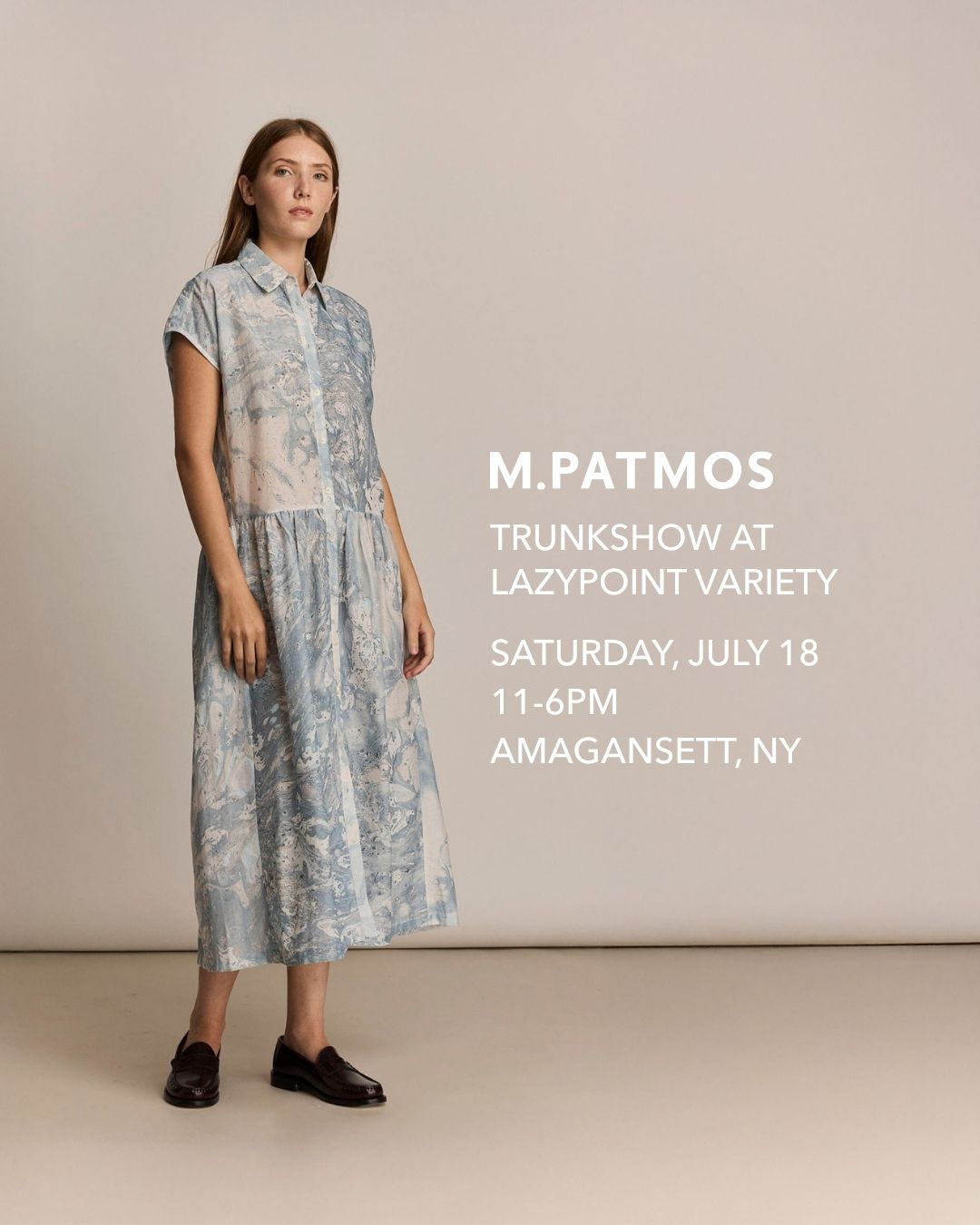 A model stands against a plain beige studio background wearing a light blue and white patterned midi dress with short sleeves and dark loafers. 