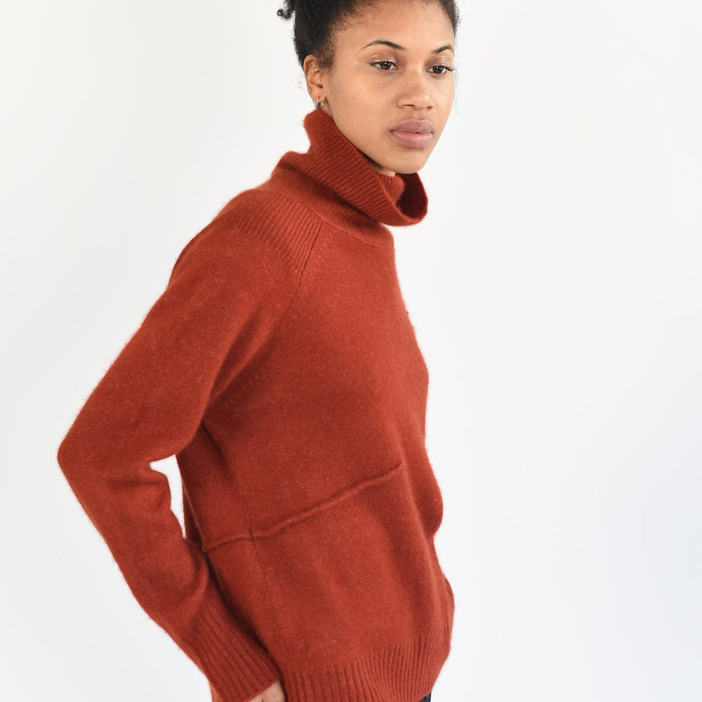 
                  
                    A woman wearing a rust-colored turtleneck sweater with raglan sleeves and a ribbed yoke, made from cashmere silk yarn.
                  
                