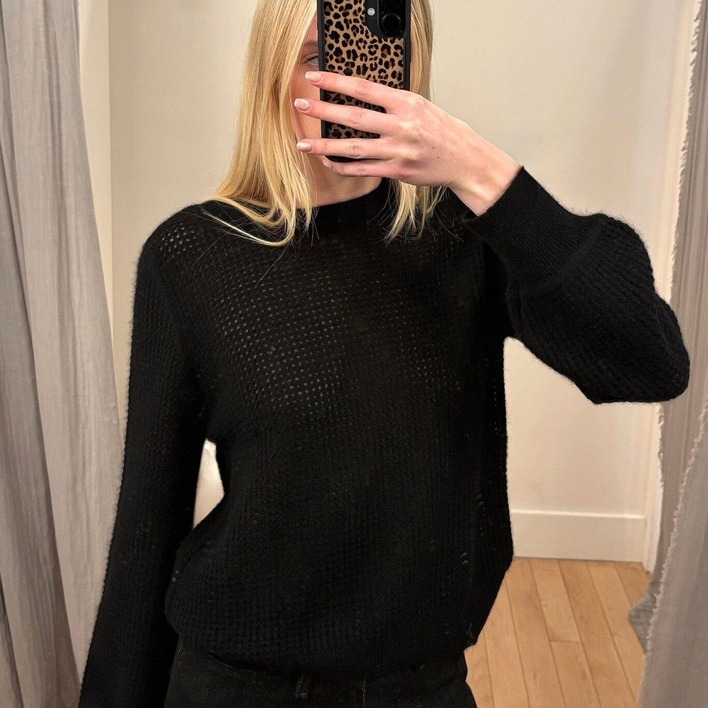 A woman wearing a black mesh knit sweater taking a mirror selfie.
