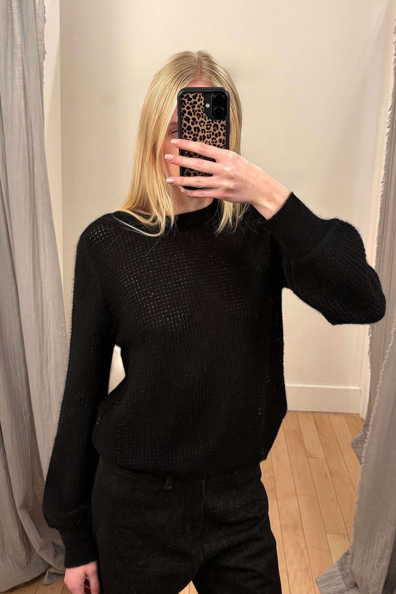 A woman wearing a black mesh knit sweater taking a mirror selfie.