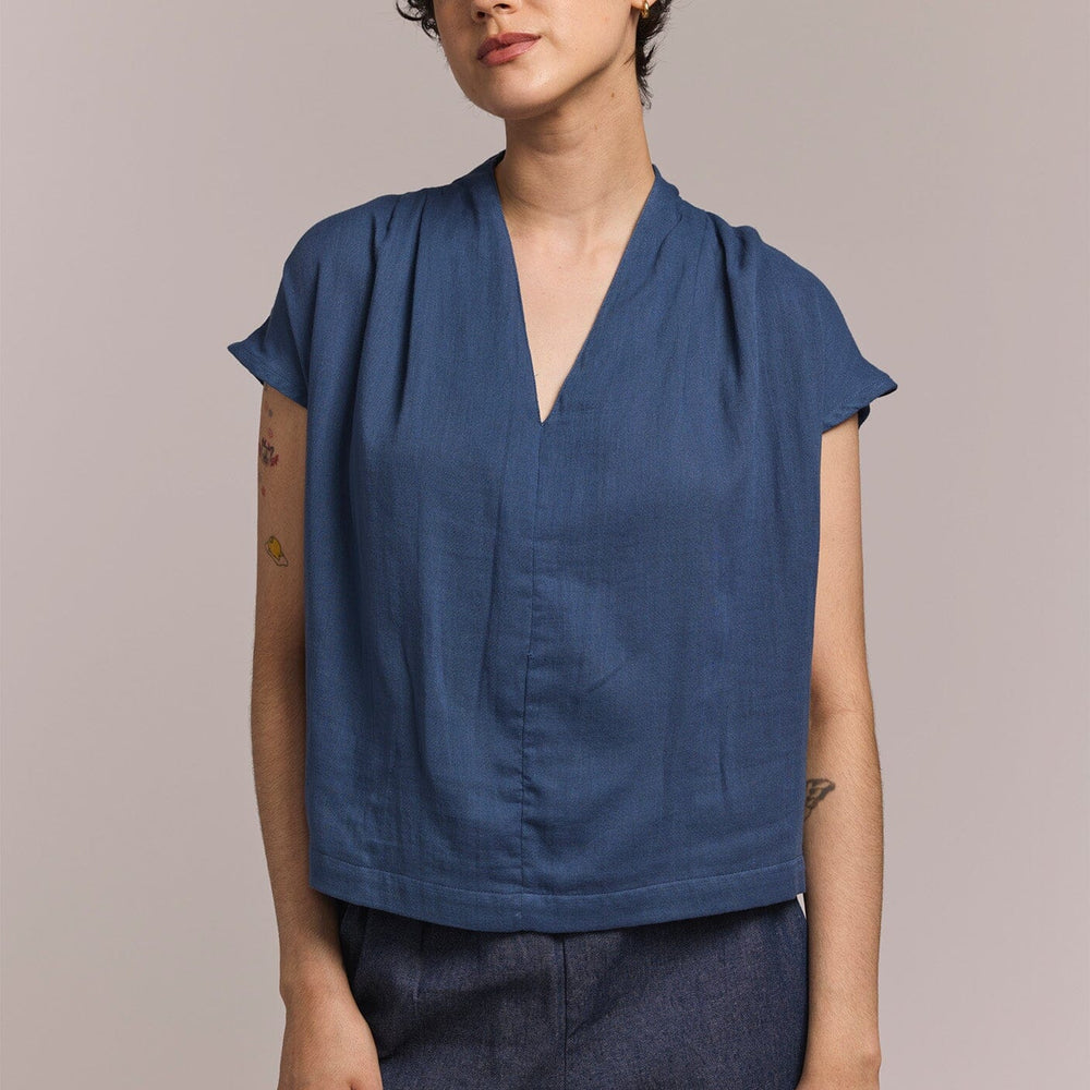 
                  
                    Person wearing a blue top and dark pants against a plain background
                  
                