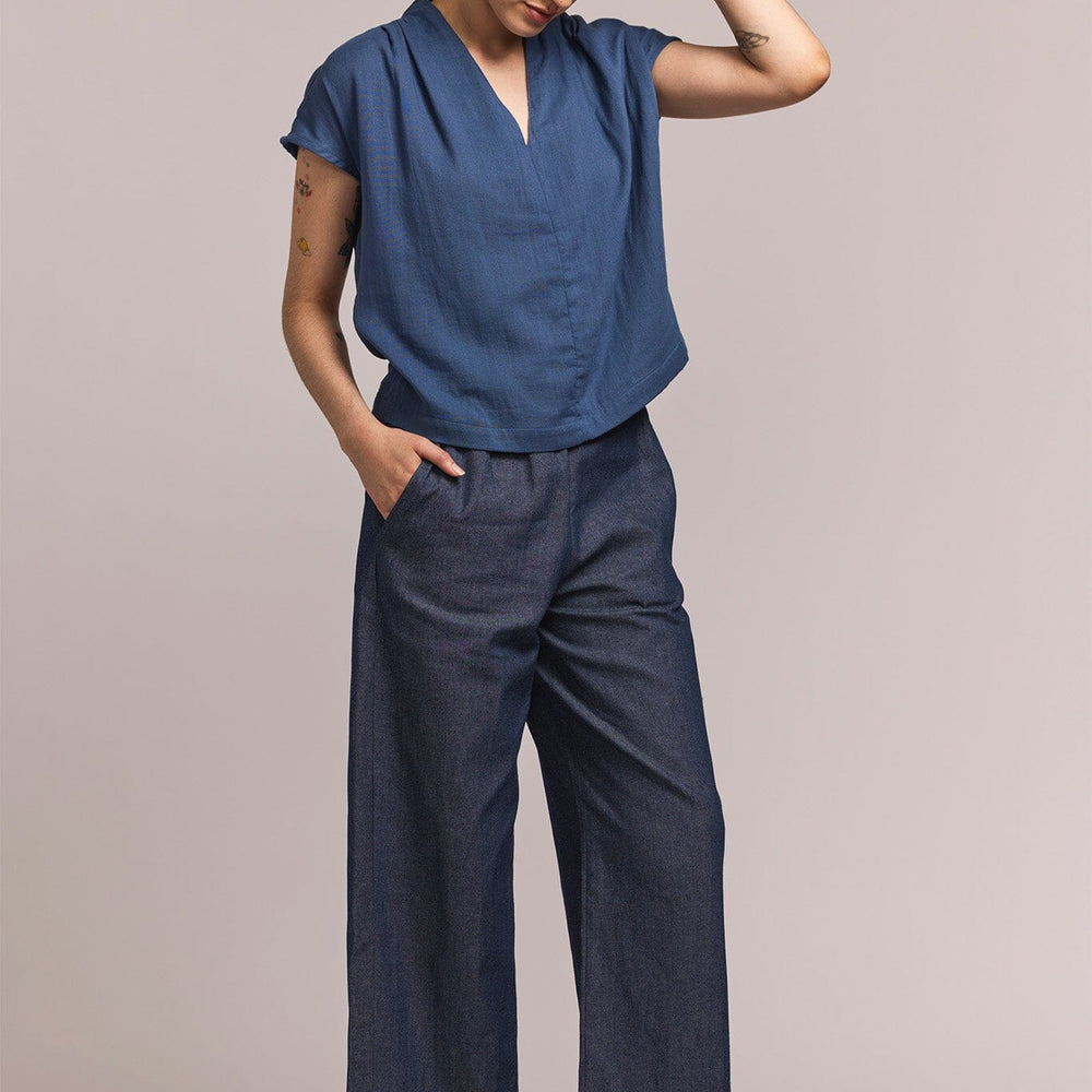 
                  
                    Person wearing a blue v-neck blouse with denim pants against a plain background
                  
                