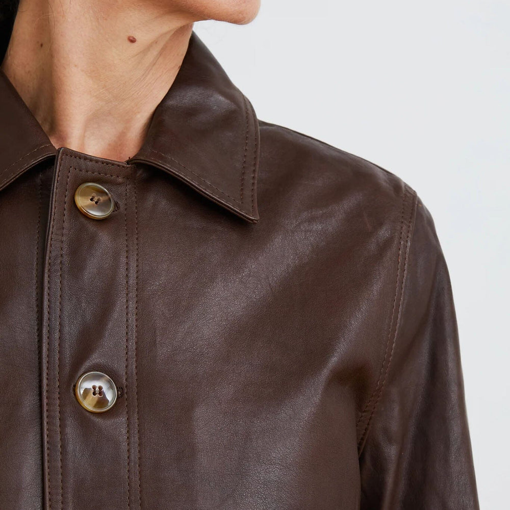 
                  
                    Close-up of a brown leather jacket with gold buttons on a plain background
                  
                