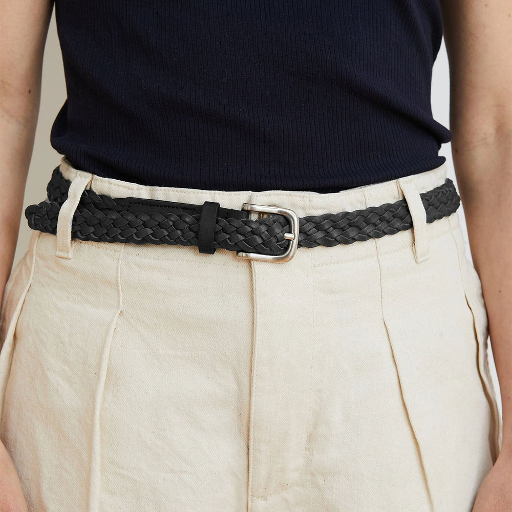 Person wearing a black woven belt with beige pants against a neutral background