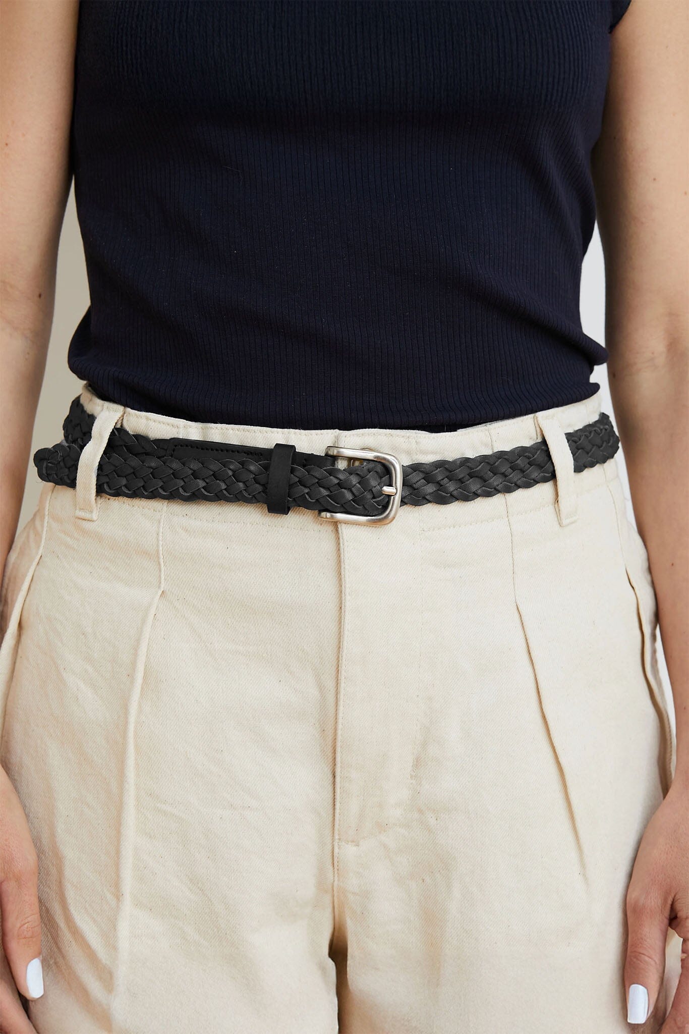 Person wearing a black woven belt with beige pants against a neutral background
