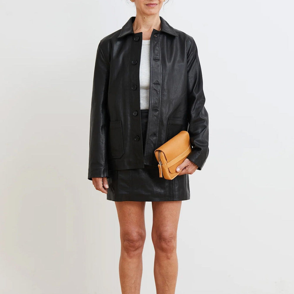 Woman wearing a black jacket and skirt with a yellow clutch against a white background