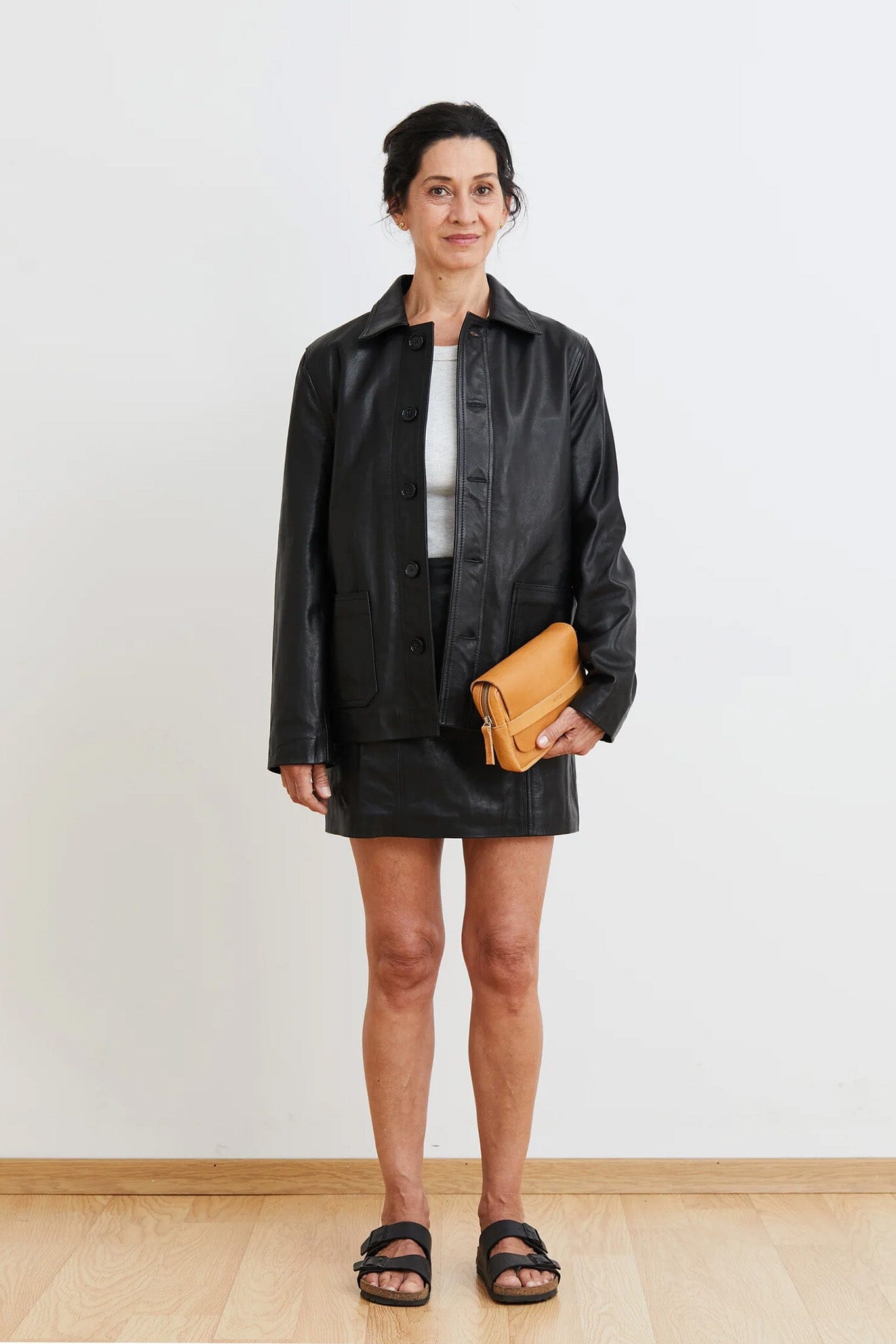 Woman wearing a black jacket and skirt with a yellow clutch against a white background