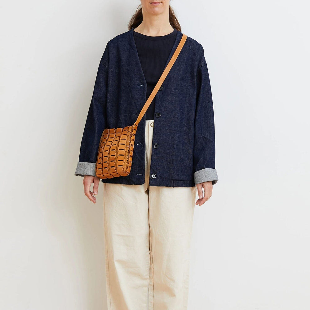 Woman wearing a navy jacket and beige pants with a brown bag against a white wall.