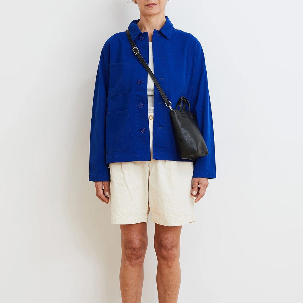 Person wearing a blue jacket and white shorts standing against a plain background