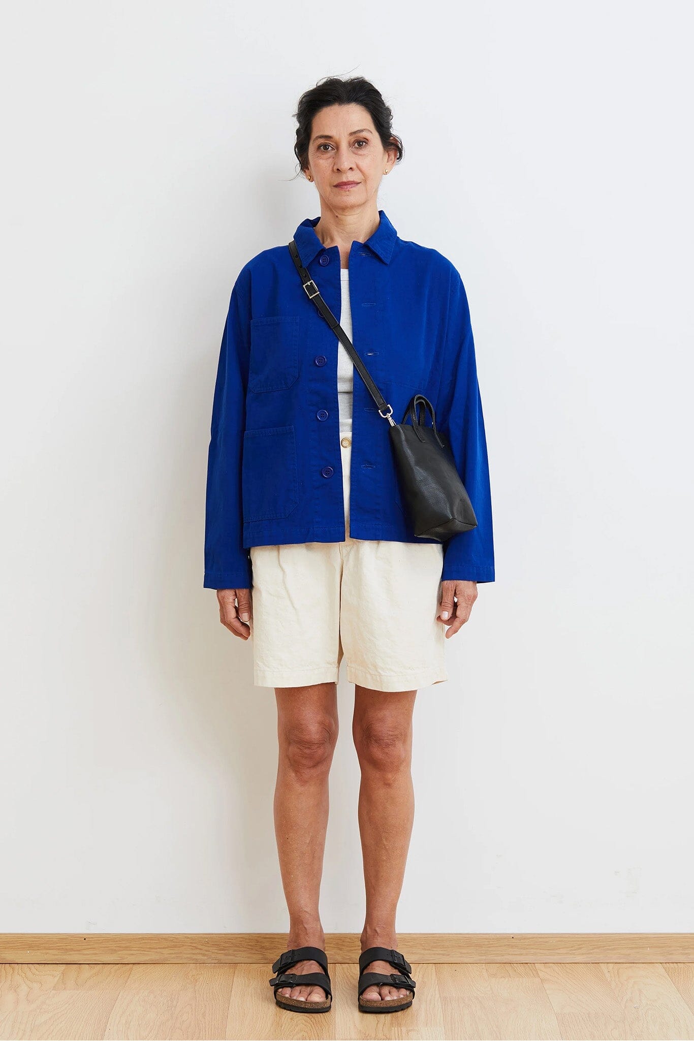 Person wearing a blue jacket and white shorts standing against a plain background