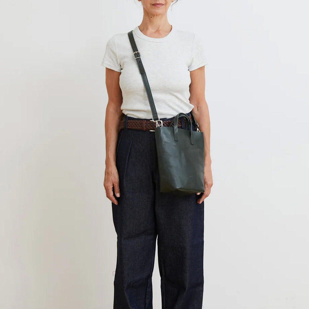 
                  
                    Person wearing a white t-shirt, dark pants, and carrying a green bag against a plain background
                  
                