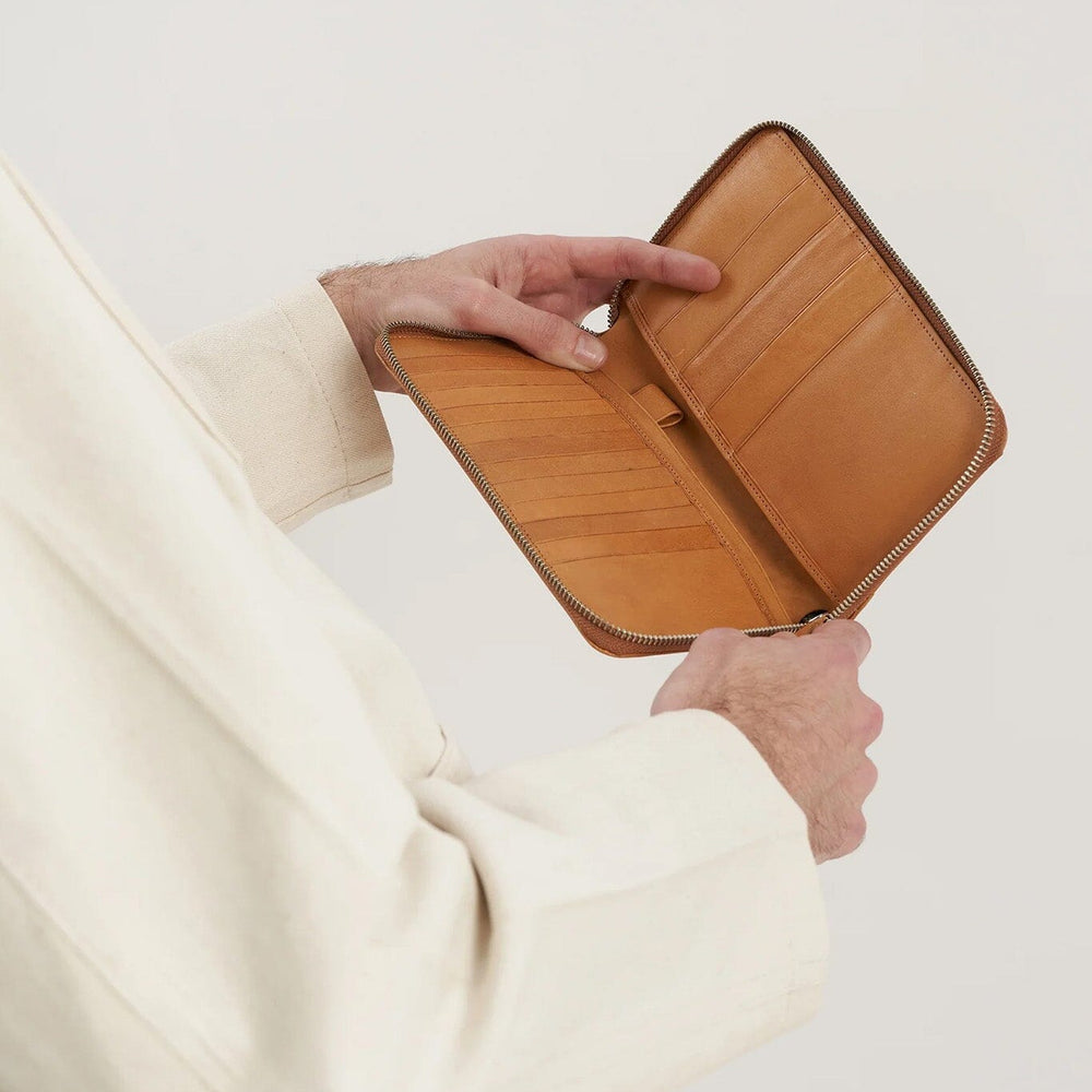 
                  
                    Person holding a tan wallet against a neutral background
                  
                