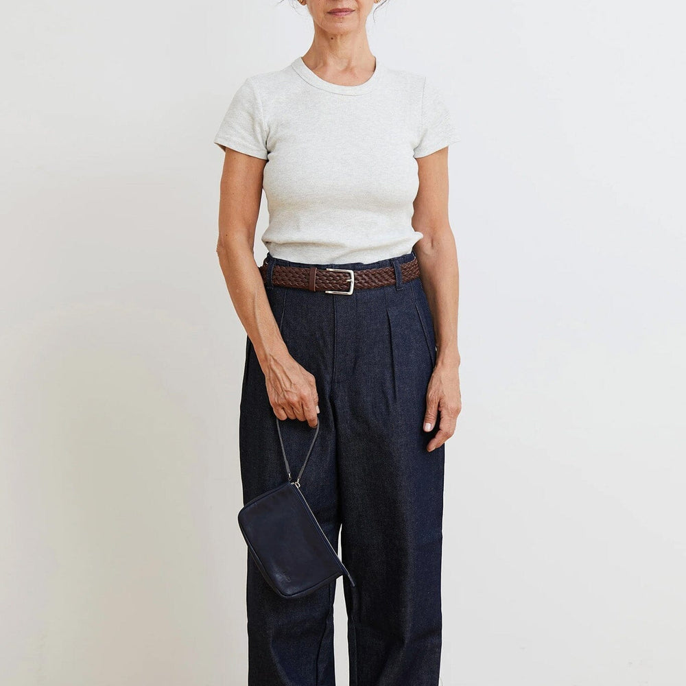 Woman wearing a white t-shirt and navy pants holding a navy zipper pouch against a plain background