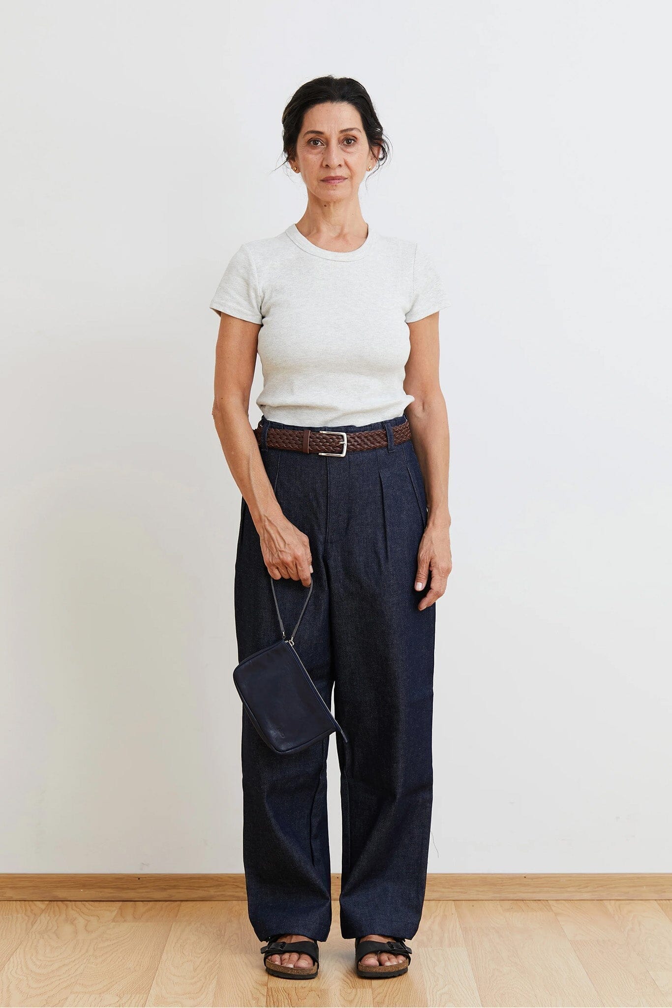 Woman wearing a white t-shirt and navy pants holding a navy zipper pouch against a plain background
