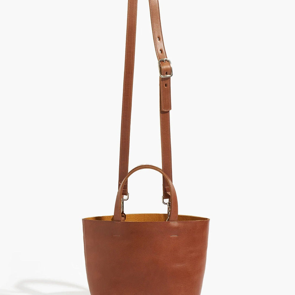 
                  
                    Brown leather tote bag with a strap on a white background
                  
                