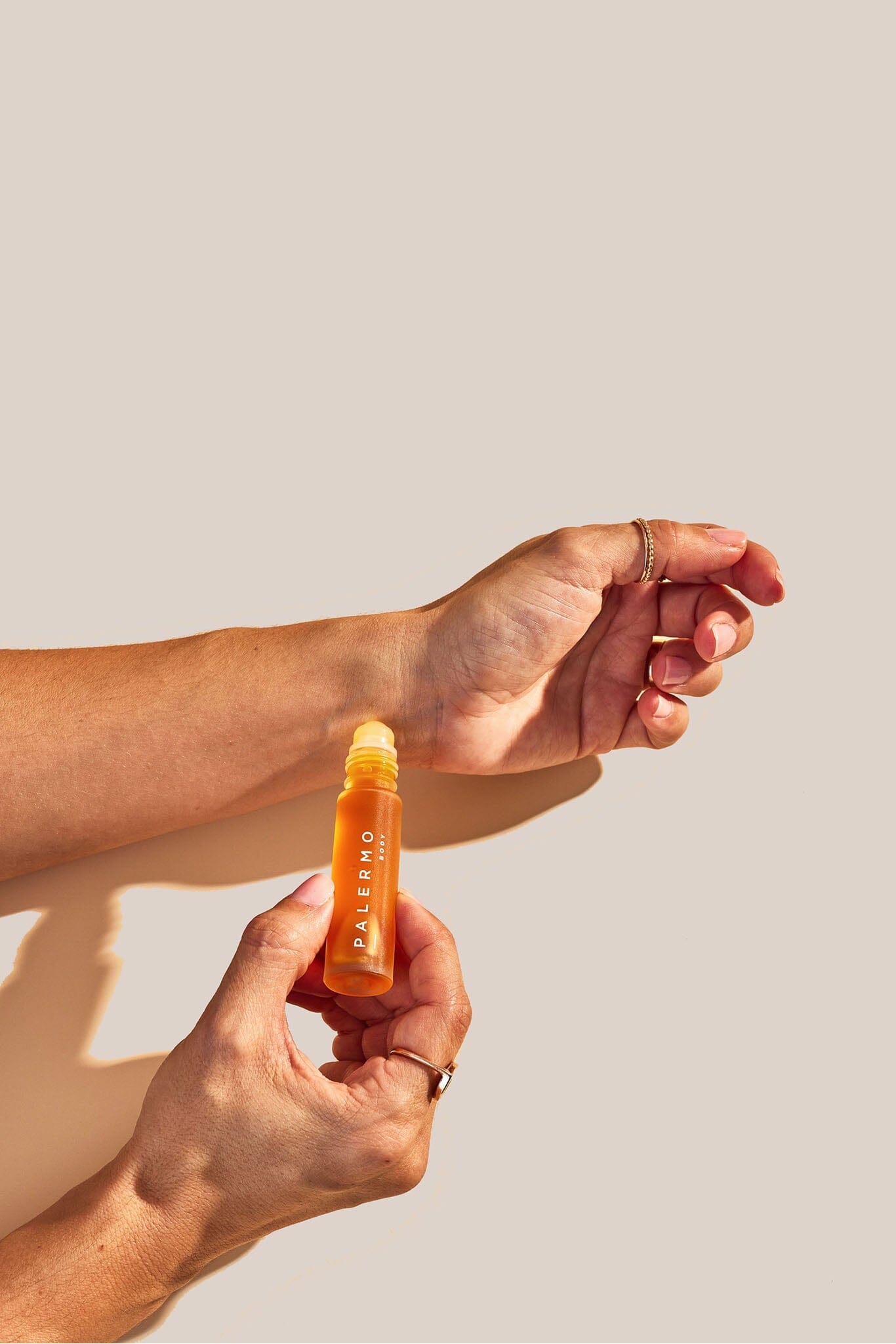 Two hands holding a perfume bottle labeled 'Palermo' against a beige background