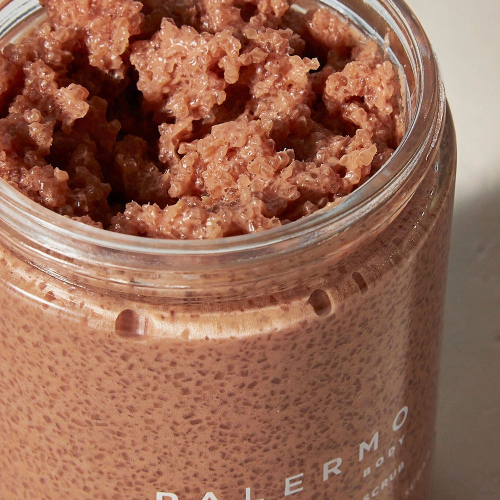 A close up of a jar containing a pinkish body scrub with exfoliants, labeled 'PALERMO BODY' on the front.