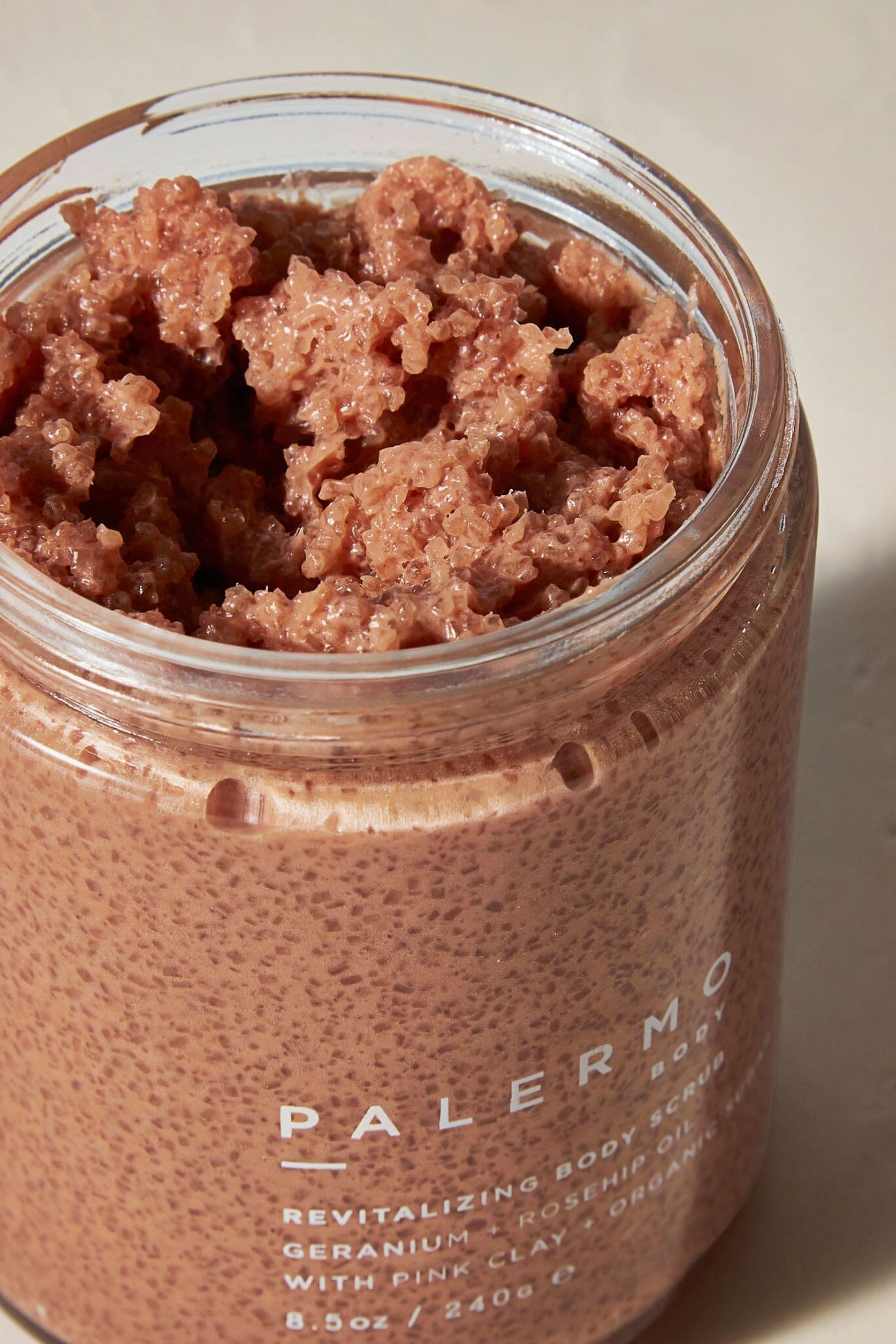 A close up of a jar containing a pinkish body scrub with exfoliants, labeled 'PALERMO BODY' on the front.