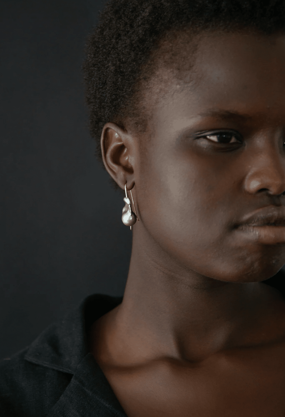 Close-up of a person wearing pearl earrings against a dark background
