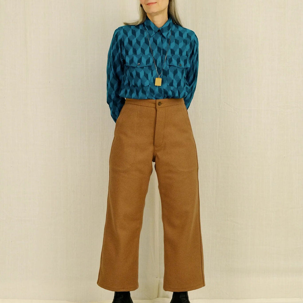 Woman wearing a blue patterned shirt and brown pants against a plain background