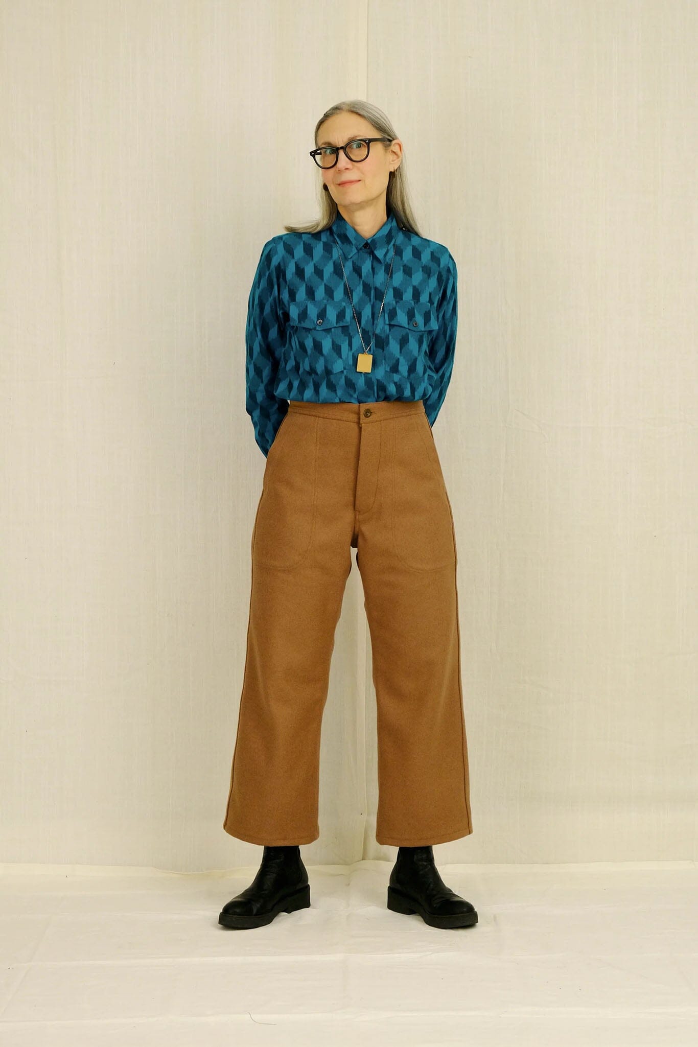 Woman wearing a blue patterned shirt and brown pants against a plain background