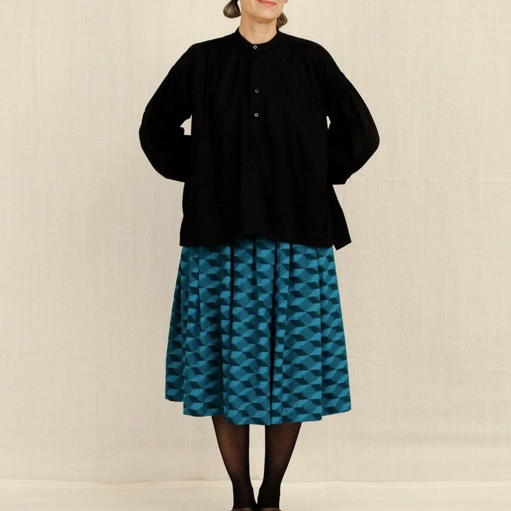 Person wearing a black jacket and blue patterned skirt on a plain background