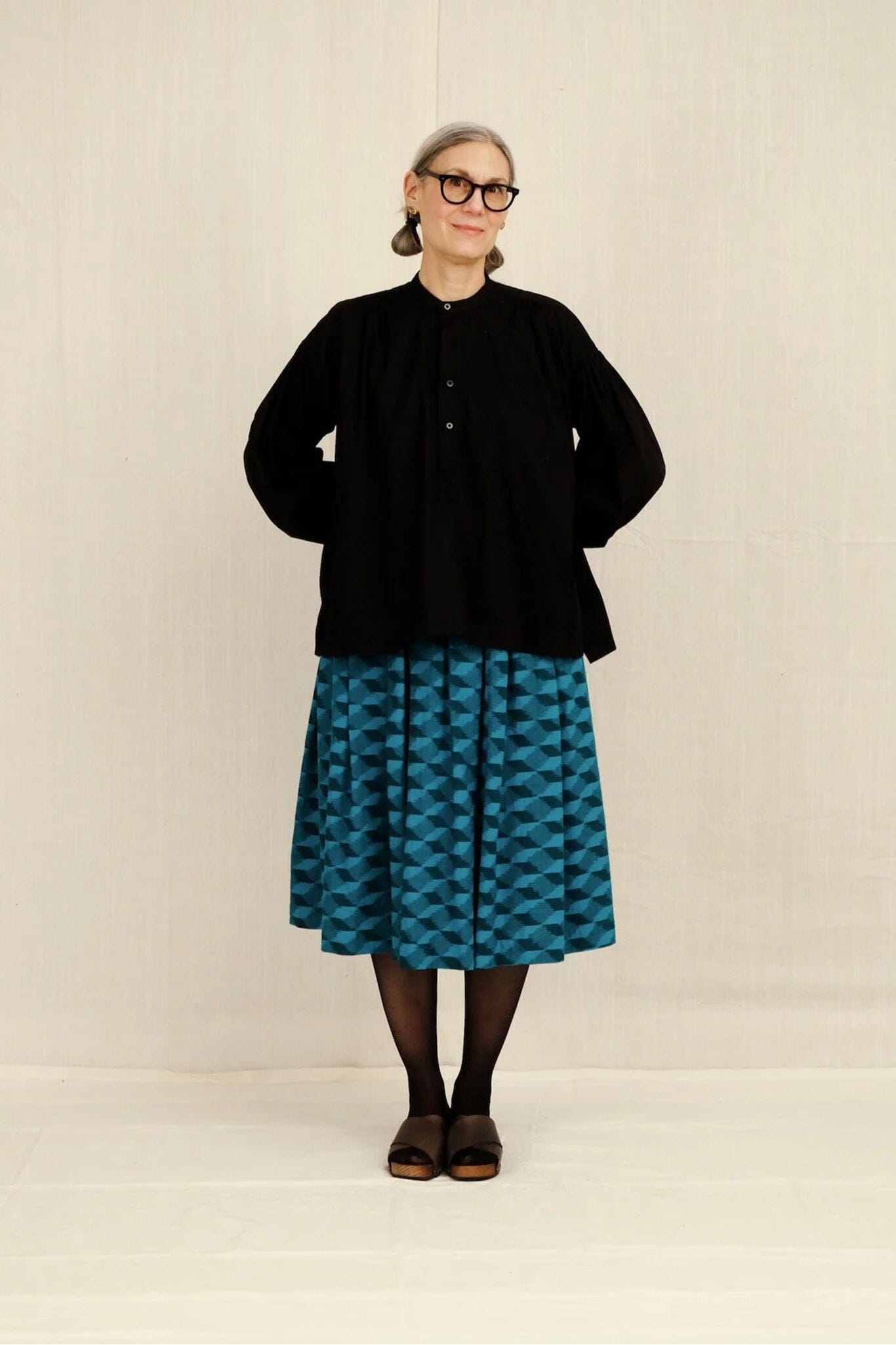 Person wearing a black jacket and blue patterned skirt on a plain background