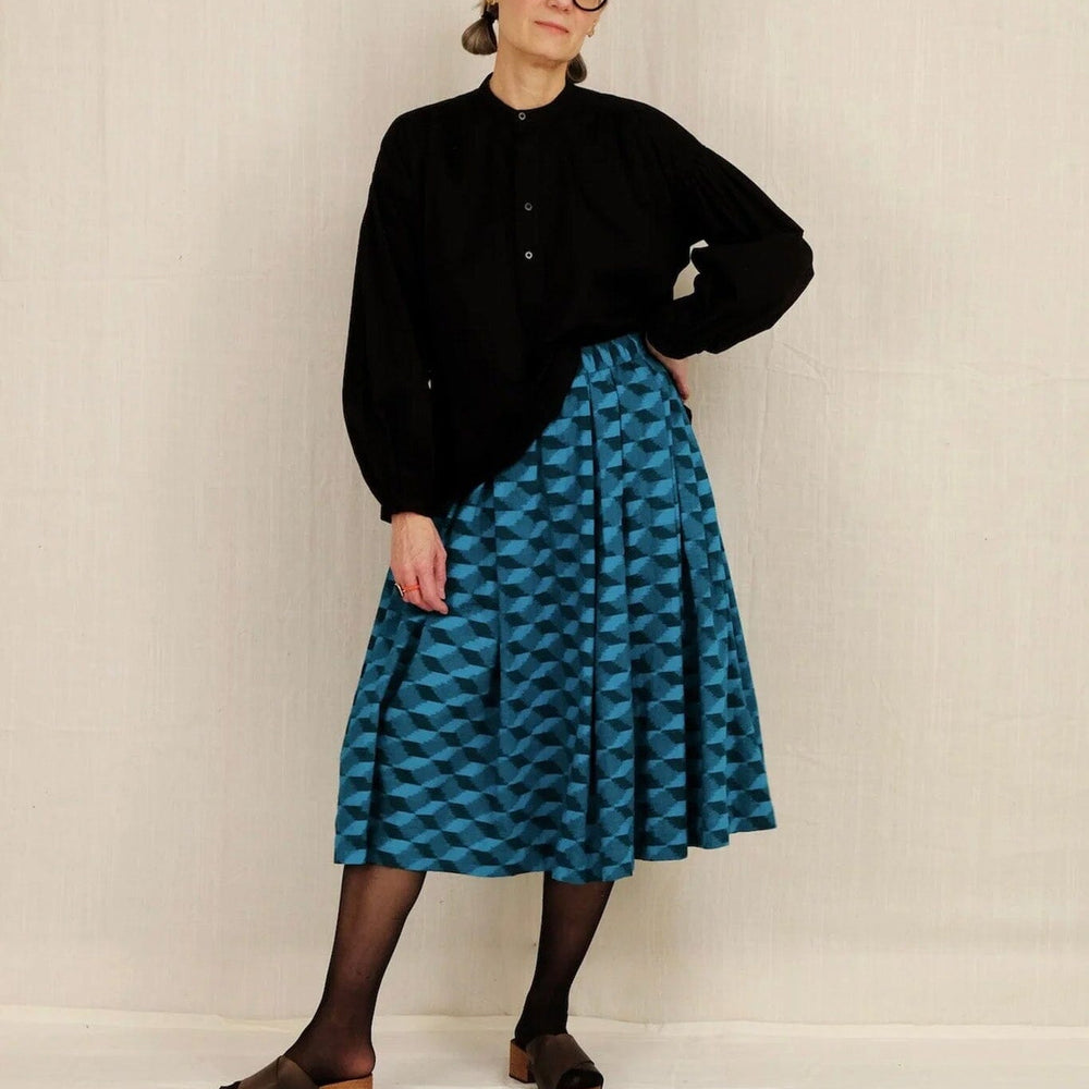 Person wearing a black sweater and blue patterned skirt against a white background