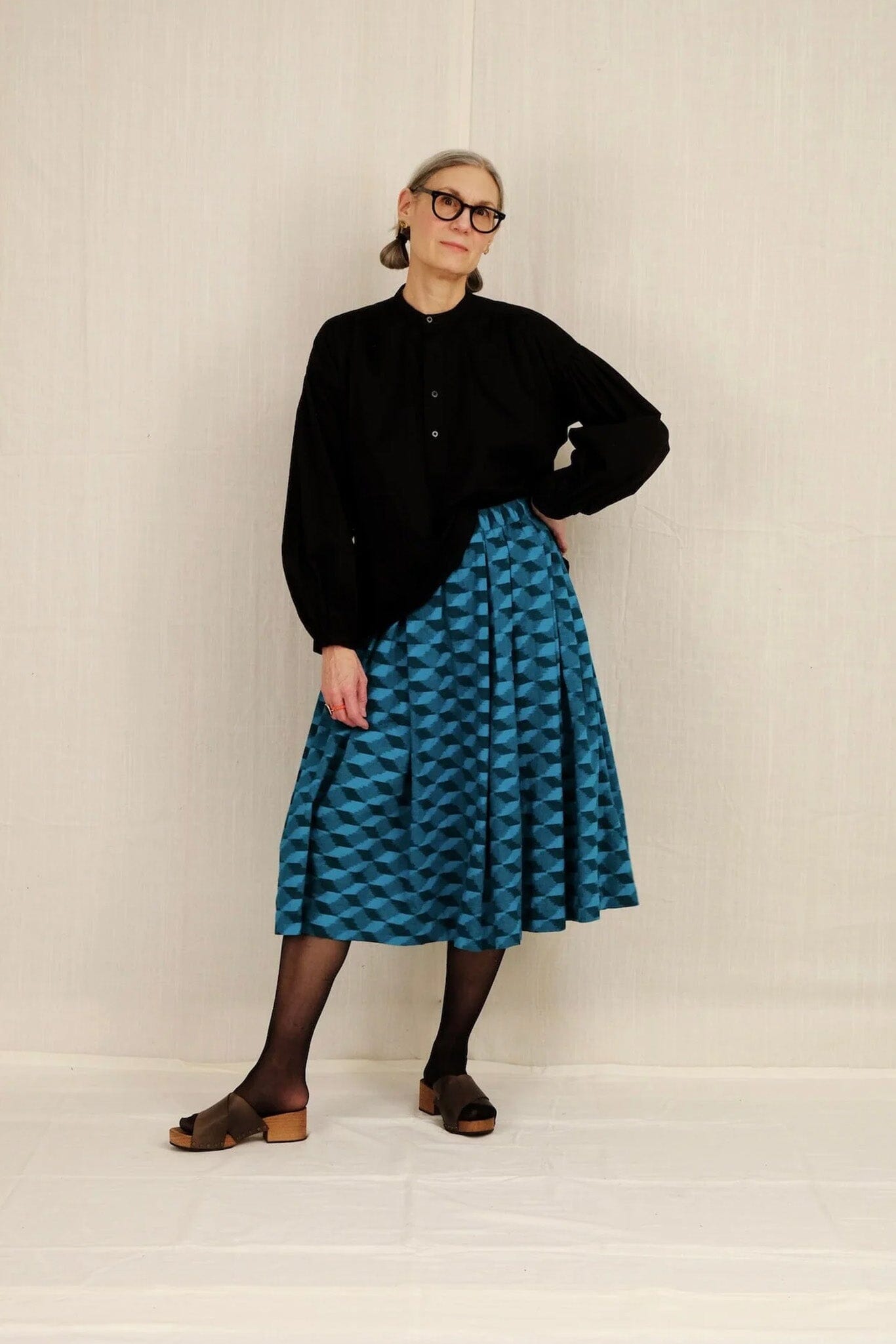 Person wearing a black sweater and blue patterned skirt against a white background
