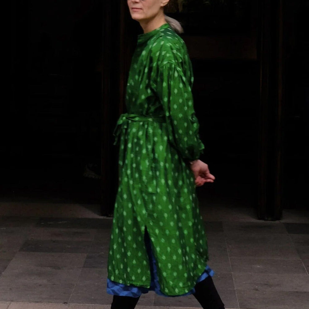 Person wearing a green patterned dress with black shoes in an indoor setting