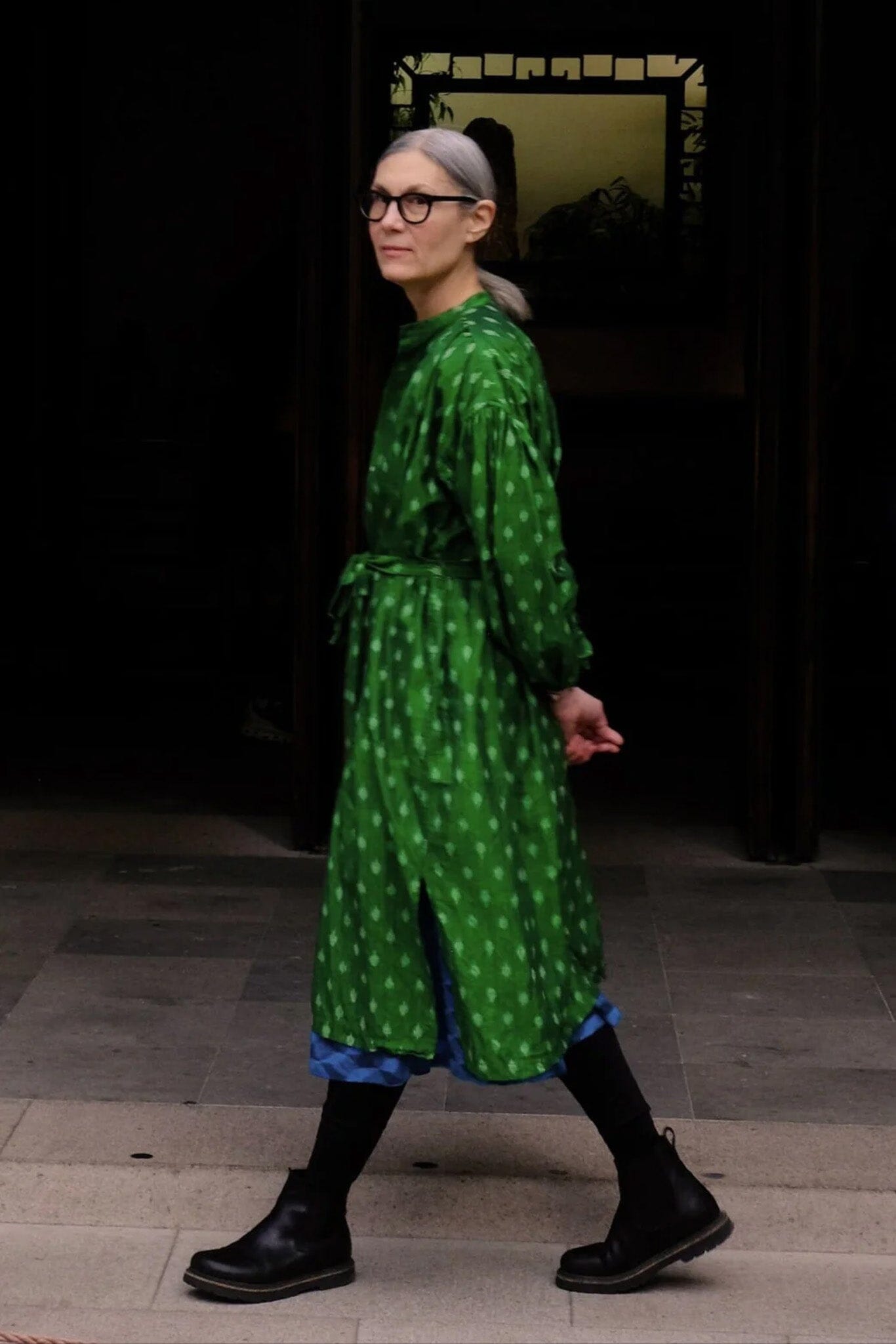 Person wearing a green patterned dress with black shoes in an indoor setting