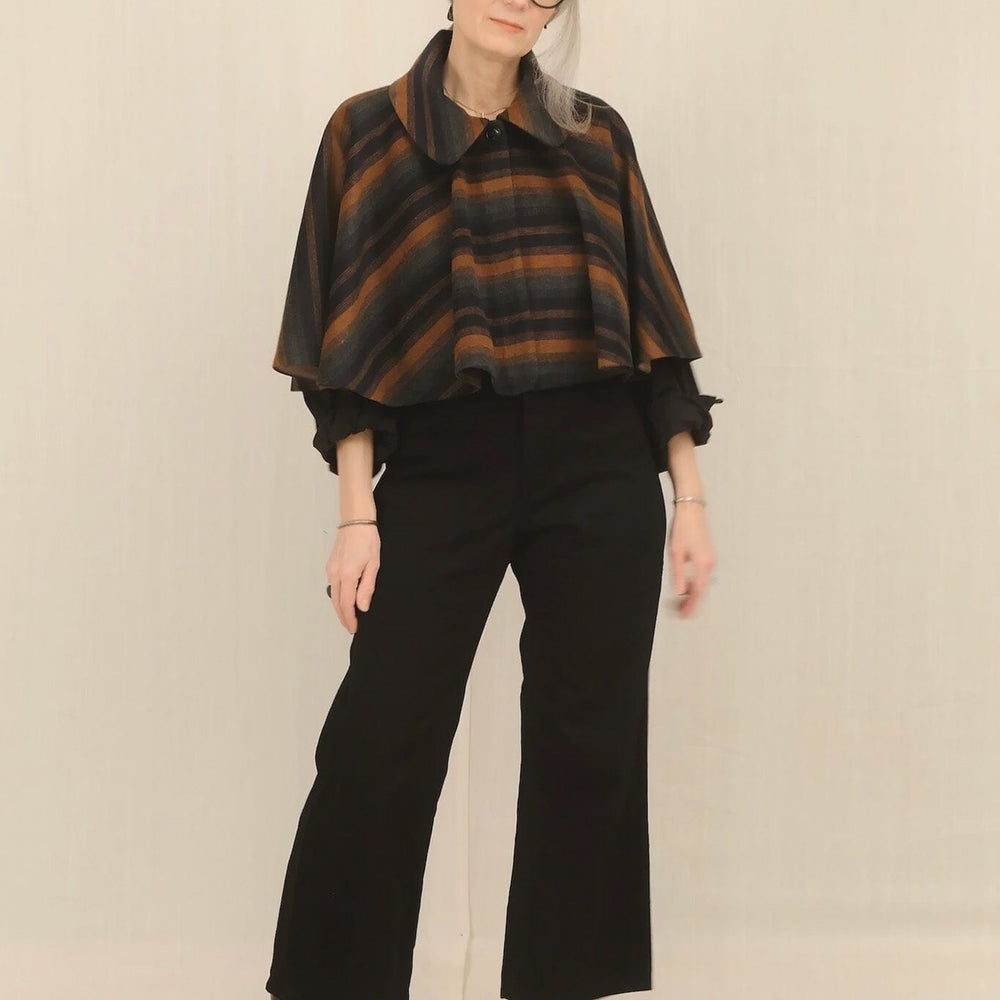 Person wearing a plaid poncho and black pants against a plain background