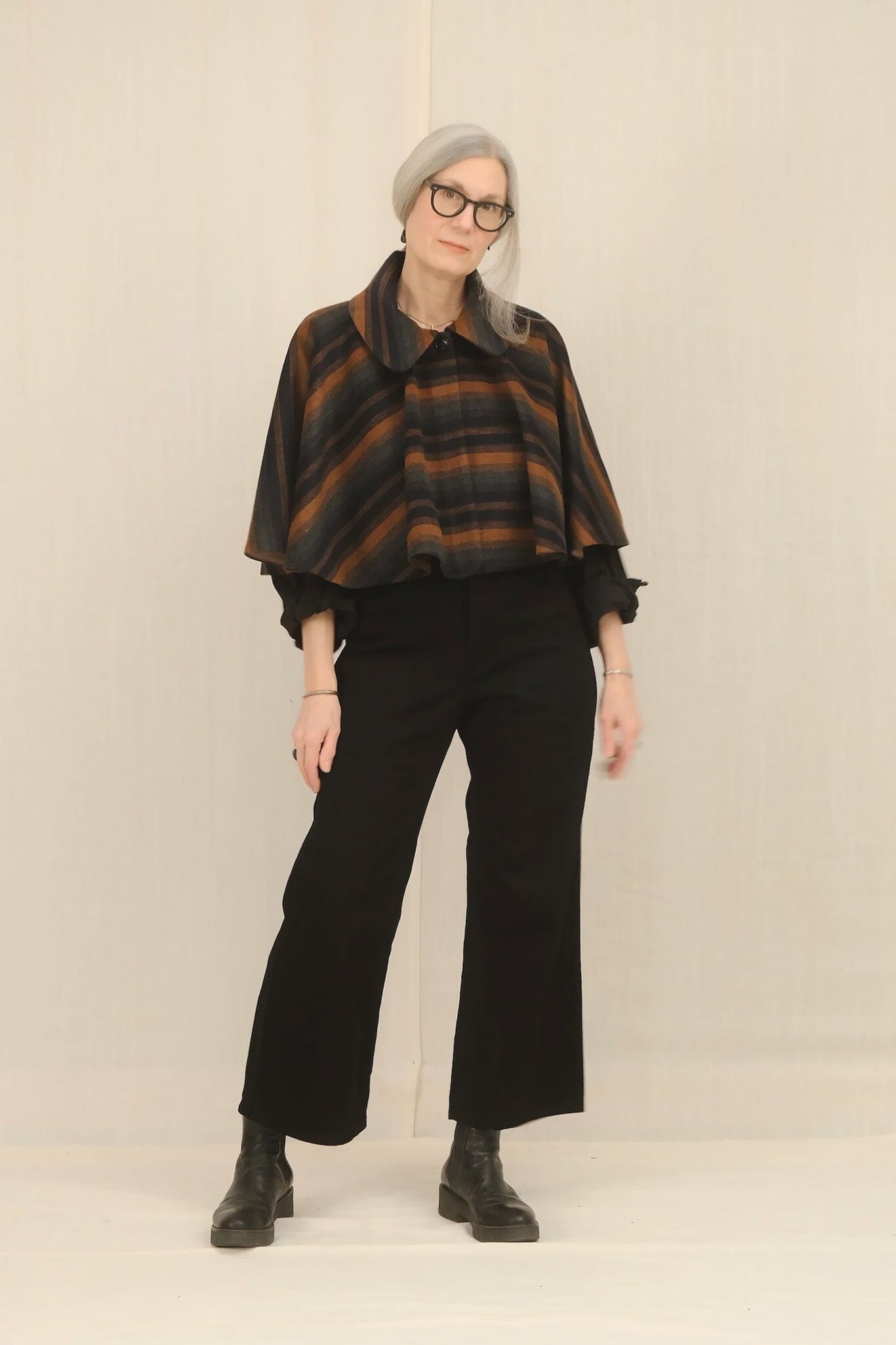 Person wearing a plaid poncho and black pants against a plain background