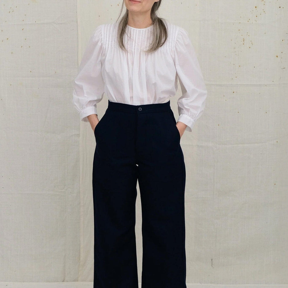 Person wearing a white blouse and dark navy pants against a plain background